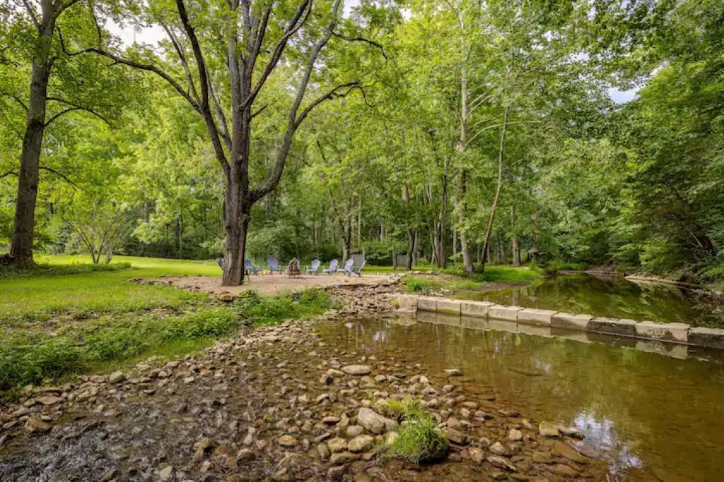 A serene outdoor area with a pond, trees, and a seating area with chairs.