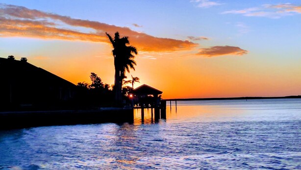 Panorama al tramonto su un bacino d'acqua tranquillo, con un molo che si estende nell'acqua, che presenta una piccola struttura e palme.