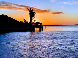 A sunset view over a calm body of water with a pier extending into the water, featuring a small structure and palm trees. - Prime Marco location with awesome view. (Marco Island)