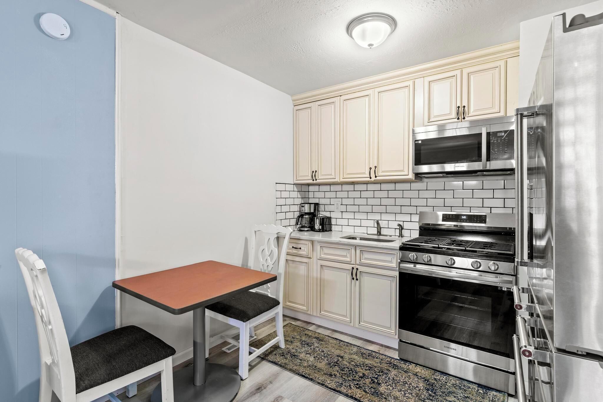 A compact kitchen with white cabinets, a stainless steel refrigerator, a microwave, and a double oven.