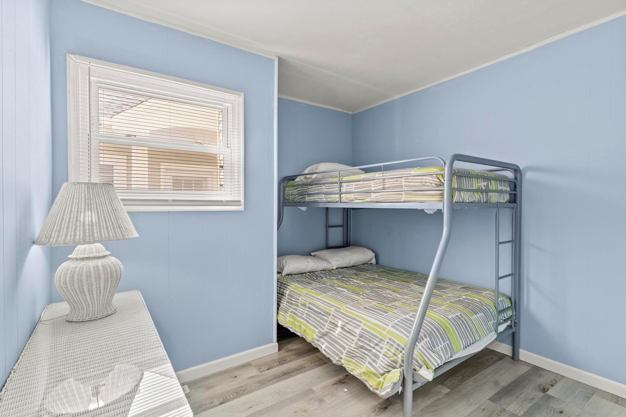 Une chambre avec un lit superposé, une lampe et une fenêtre avec des stores.
