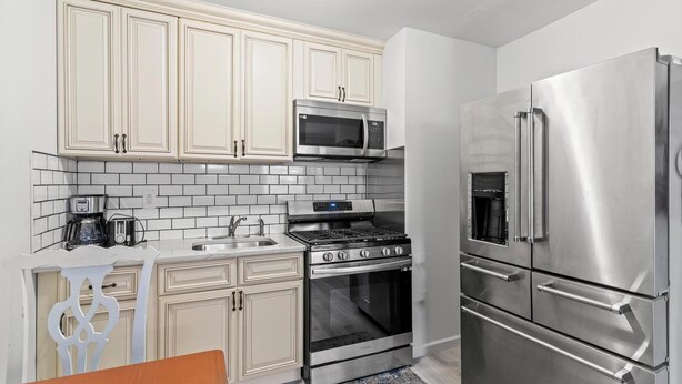 Cocina compacta con armarios blancos, refrigerador de acero inoxidable, microondas, estufa y pileta.
