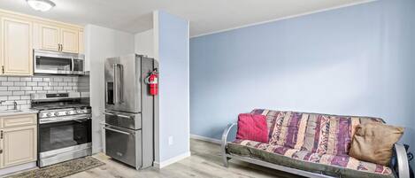 Una cocina compacta con electrodomésticos modernos, un sofá con cojines estampados y un extintor de incendios en la pared.
