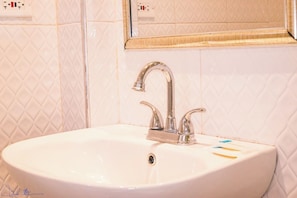 Une salle de bain avec un lavabo blanc, un miroir au-dessus et un mur recouvert de carreaux.