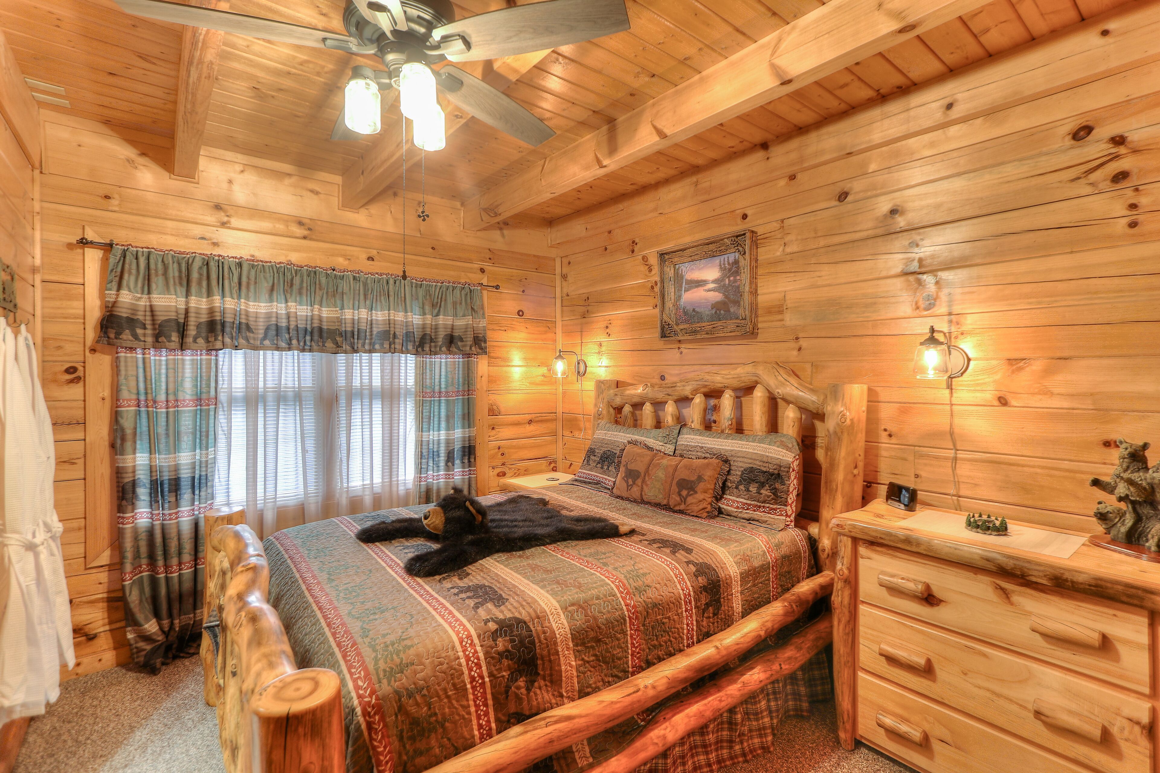 Een houten slaapkamer met een bed, nachtkastje, dressoir, plafondventilator en een schilderij aan de muur.