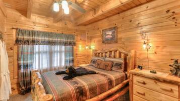 Een houten slaapkamer met een bed, nachtkastje, dressoir, plafondventilator en een schilderij aan de muur.