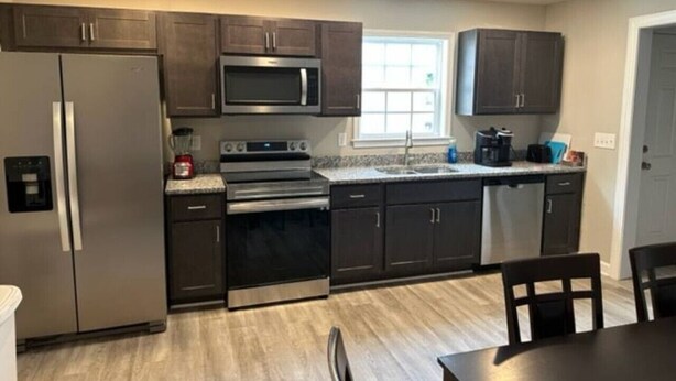 A modern kitchen with dark cabinetry, stainless steel appliances, and a window providing natural light. - Holy Holt of Lexington nc (Lexington)