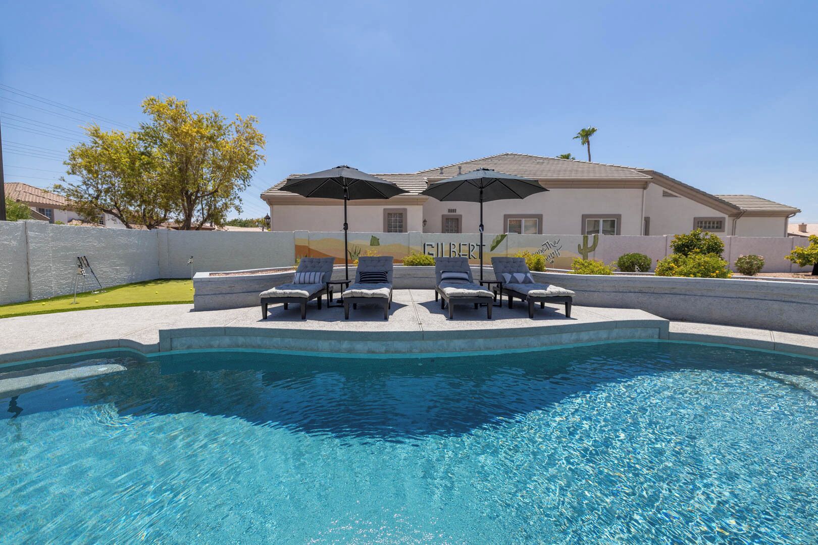 A swimming pool with lounge chairs and umbrellas, surrounded by a landscaped area and a building with a mural.