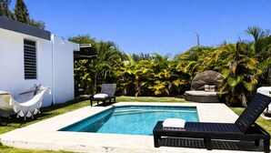 A swimming pool with lounge chairs, a hammock, and tropical plants.