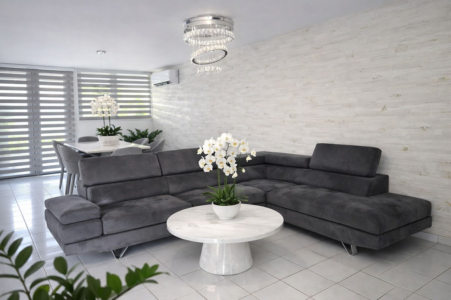 A modern living room with a grey sectional sofa, a white marble coffee table, and a chandelier.
