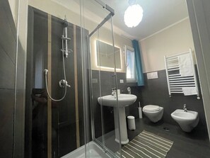 Une salle de bain moderne avec une douche à parois de verre, un lavabo sur colonne, des toilettes et un bidet.