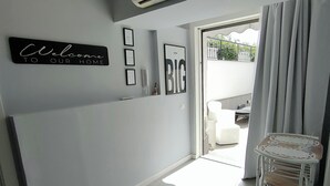 Una sala de estar moderna con una pared gris, un letrero de bienvenida negro, un cuadro enmarcado y una pequeña mesa blanca.