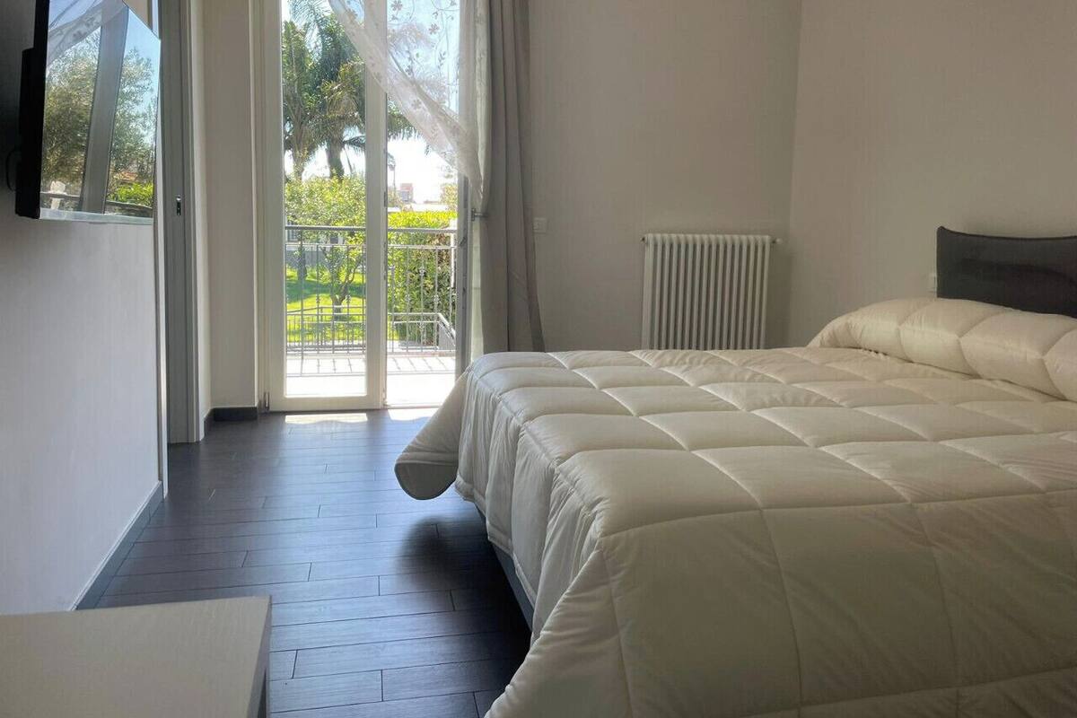 Une chambre dotée d’un grand lit, d’un téléviseur fixé au mur et d’une porte-fenêtre coulissante donnant sur un balcon.