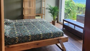 A modern bedroom with a bed, a wooden wardrobe, a potted plant, and a balcony with a mountain view. - Guest apartment with breathtaking lake view in the Swiss mountains (Seelisberg)