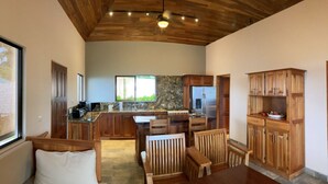 A spacious kitchen with wooden cabinets, a central island, and a dining area with wooden furniture. - Casa Ceibosito (Tres Rios de Osa)