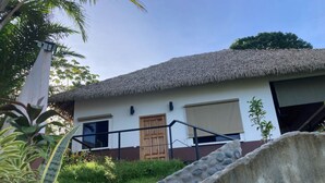 A building with a thatched roof, a wooden door, and a concrete structure in the foreground. - Casa Ceibosito (Tres Rios de Osa)