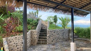 A stone staircase leading up to a thatched-roof structure surrounded by lush greenery. - Casa Ceibosito (Tres Rios de Osa)