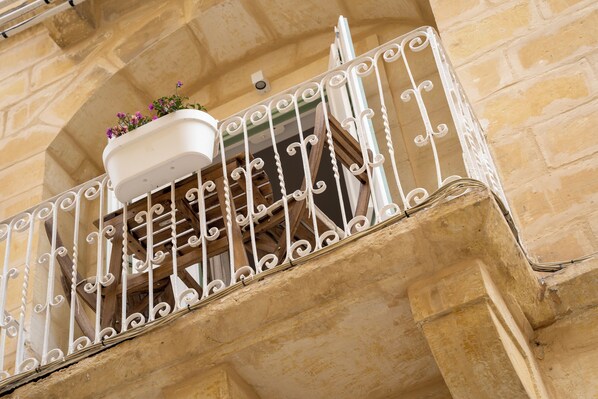 A balcony with a white wrought iron railing, a white planter box with flowers, and a stone building facade.