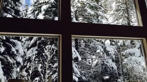 Ein Zimmer mit großen Fenstern und Blick auf schneebedeckte Bäume.