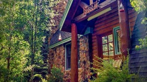 Eine rustikale Holzhütte mit einem Steinofen, einer Holzveranda und einem grünen Dach.
