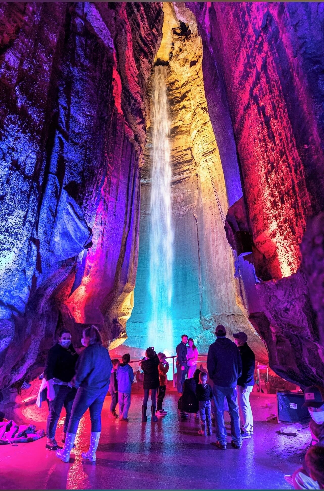 Eine Gruppe von Menschen steht vor einem Wasserfall in einer Höhle, beleuchtet mit bunten Lichtern.