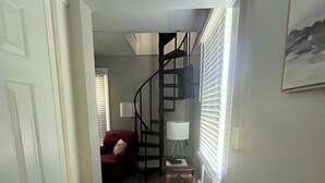 Ein Flur mit einer weißen Tür, einem roten Sofa, einer Wendeltreppe und einer Lampe.
