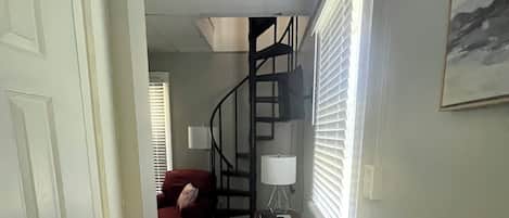 A hallway with a white door, a red couch, a spiral staircase, and a lamp.