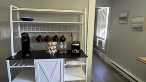 Eine Küchenzeile mit Kaffeemaschine, Wasserkocher und Toaster. Ein weißer Schrank mit Glastür und ein Regal darüber.