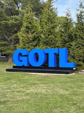 Een groot blauw bord met de letters 'GOTL' in een grasrijk gebied met bomen op de achtergrond.
