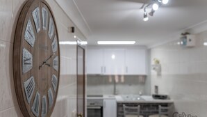 Une cuisine moderne avec une grande horloge en bois accrochée au mur, des meubles blancs et un coin repas avec des chaises.