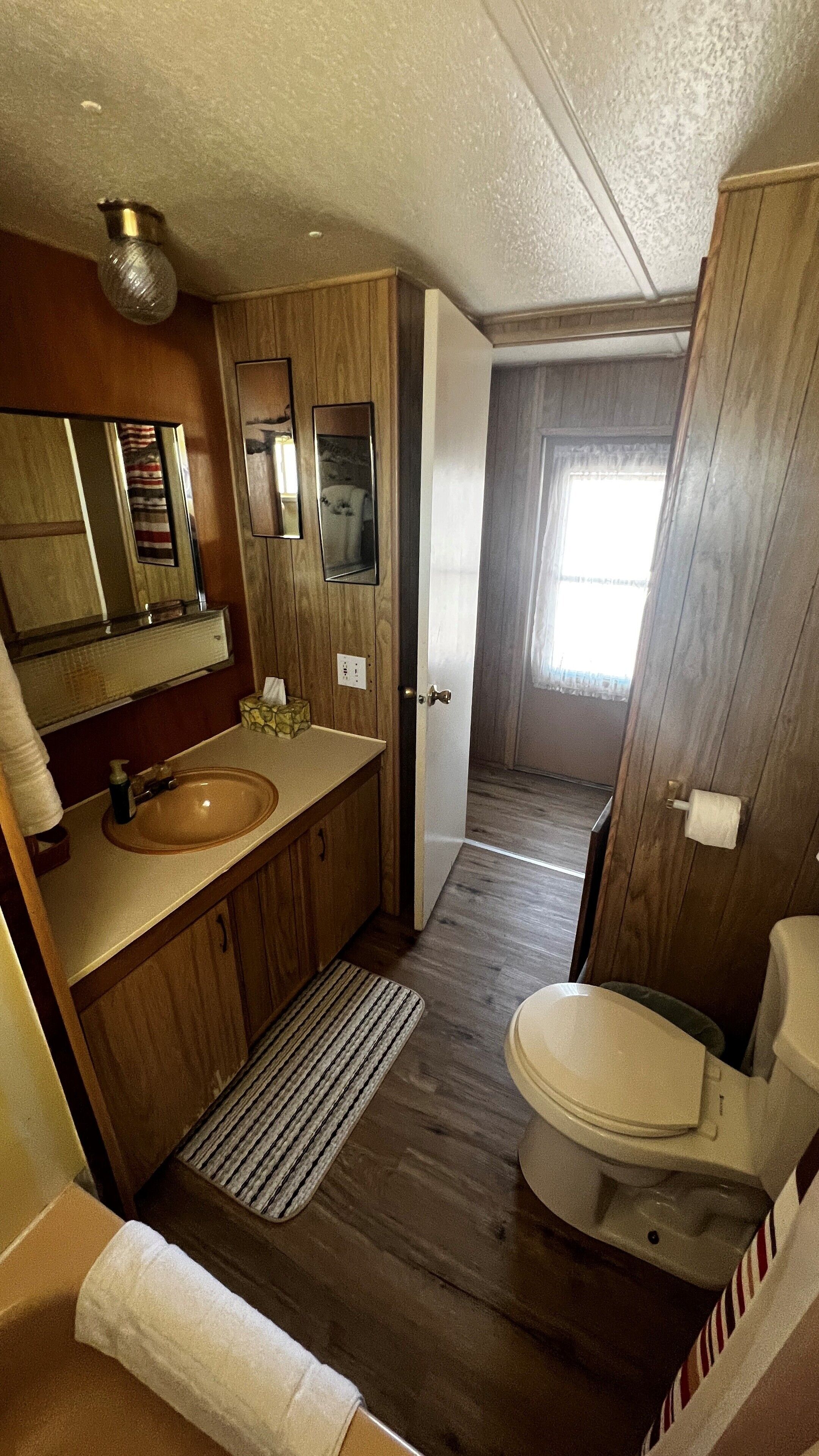 A compact bathroom with a wooden vanity, a sink, a mirror, and a toilet.
