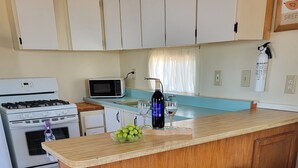 Una cocina con una isla de madera, dos taburetes, una estufa a gas, un microondas y un fregadero.