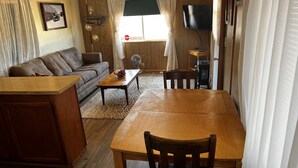 Una sala de estar con un sofá, una mesa de centro de madera, una mesa de comedor con sillas, un televisor y un pequeño calentador.
