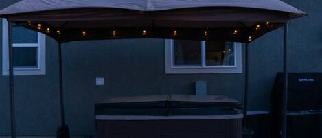 A covered outdoor area with a hot tub, a grill, and a patio umbrella.