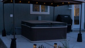 Een overdekt terras met een hottub, omgeven door een lage muur en een kleine tuin.