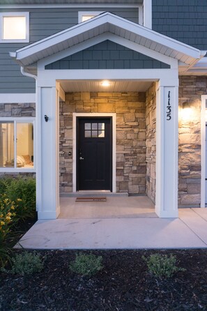 A house with a stone facade, a black front door, and a small porch with a white railing. - Heber Haven Home (Daniel)