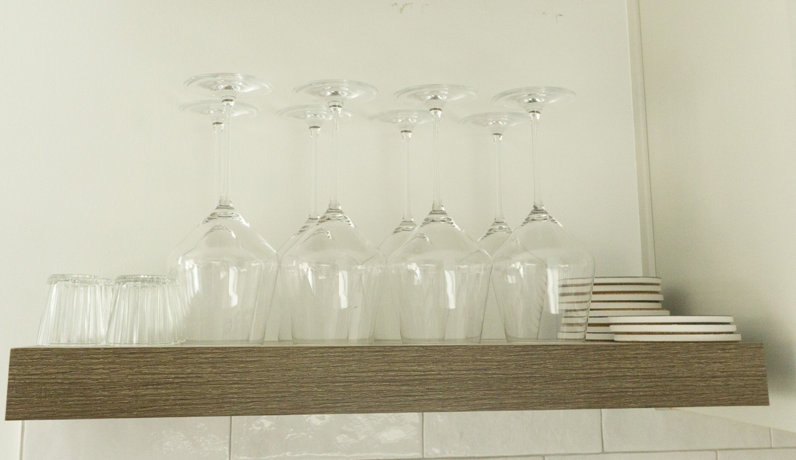 A wooden shelf with wine glasses and tumblers.