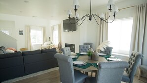 Een moderne woonkamer met een donkergrijze bank, een eettafel met grijze stoelen en een kroonluchter.