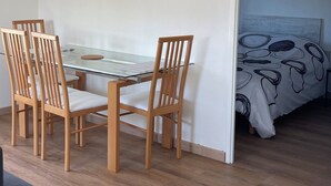 Um quarto com uma mesa de jantar de madeira e cadeiras, uma cama com colcha estampada e um relógio de parede.