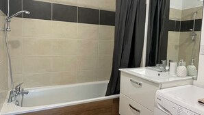 Uma casa de banho moderna com banheira, chuveiro e máquina de lavar roupa.