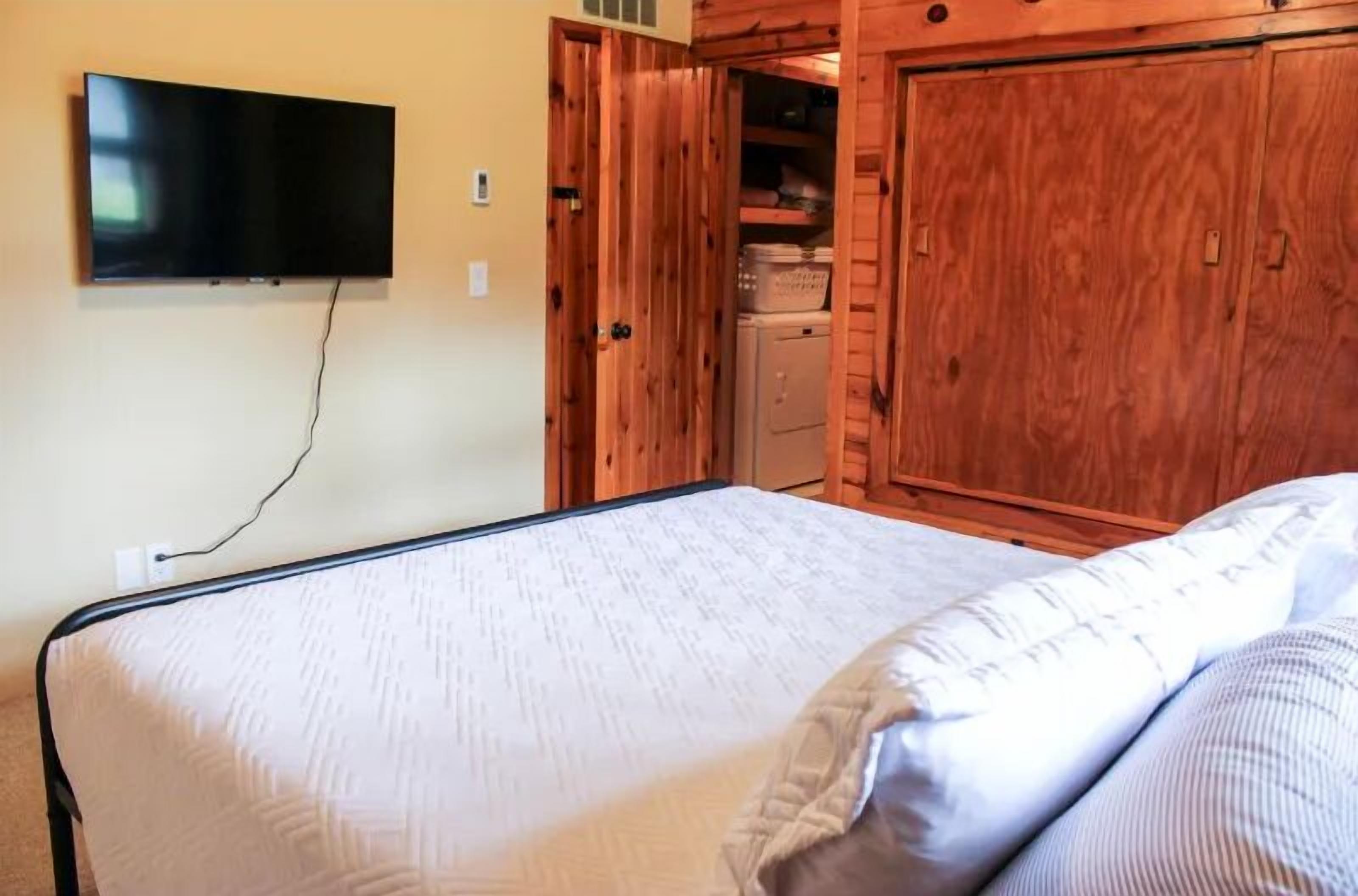 Une chambre à coucher avec un lit, un téléviseur fixé au mur et une porte en bois donnant sur un placard.