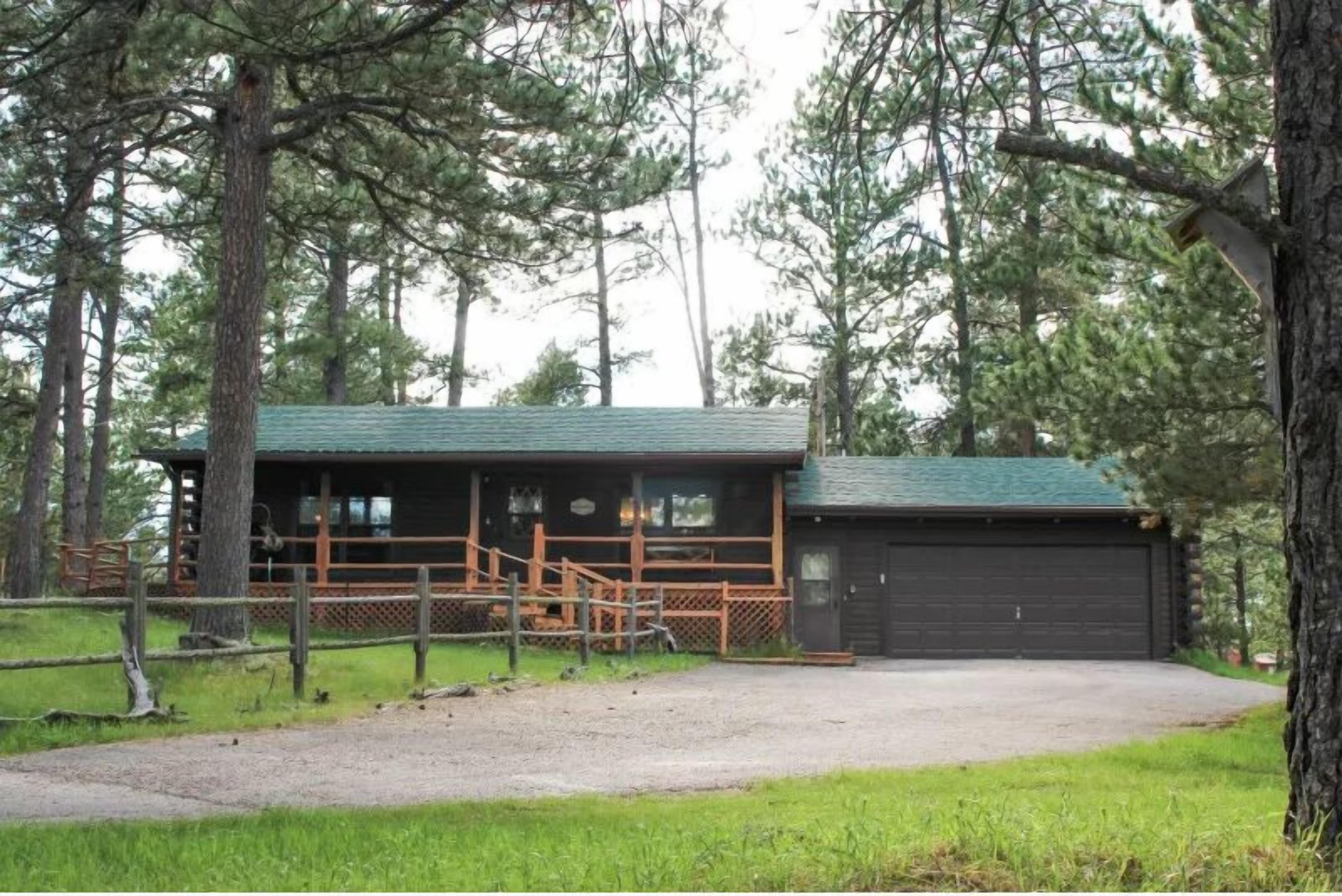 A cabin with a covered porch, a garage, and a fenced-in area.