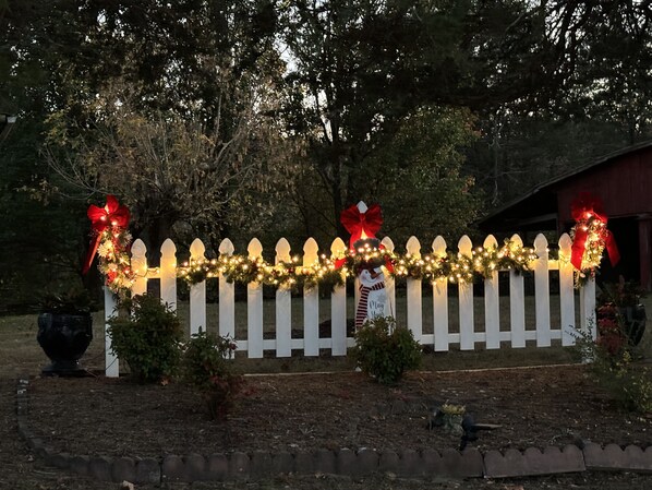 Una cerca blanca de piquetes con luces de adorno y lazos rojos, una decoración de muñeco de nieve y un cartel que dice 'May Your'.