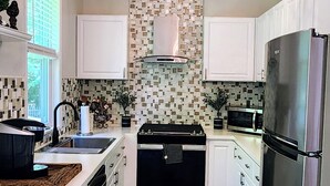 Une cuisine moderne avec des meubles blancs, un réfrigérateur en acier inoxydable, une cuisinière noire et un crédence décorée.