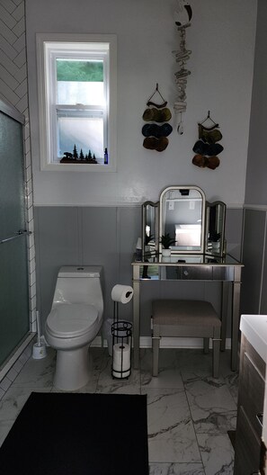 A bathroom with a toilet, sink, and mirror. There is a window with a view of trees and a bear silhouette. - Waterfront Home, 3 BR, 2 Bath, HOT TUB, Pet-Friendly, Fishing, Fire Pit
  (Murphy)