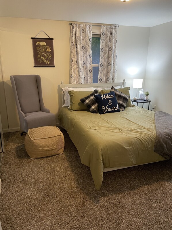 A bedroom with a bed, a chair, a small table, and a wall-mounted picture. - Cozy home close to historic Washburne District, Hospital, Autzen Stadium!  (Springfield)