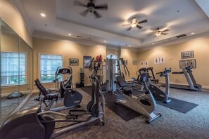 Une salle de sport équipée de divers appareils d’exercice, dotée de grandes fenêtres et de ventilateurs de plafond.