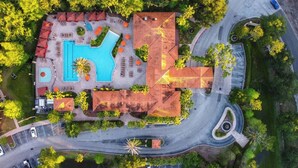 An aerial view of a resort with a swimming pool, multiple lounge areas, and a winding road.
