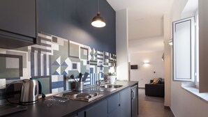 Een moderne keuken met een geometrisch achterwand, een waterkoker, een spoelbak en een zithoek met een bank.