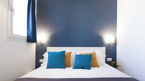 Een net opgemaakt bed met een wit hoofdbord, blauwe en mosterdkleurige kussens, en een donkerblauwe deken.